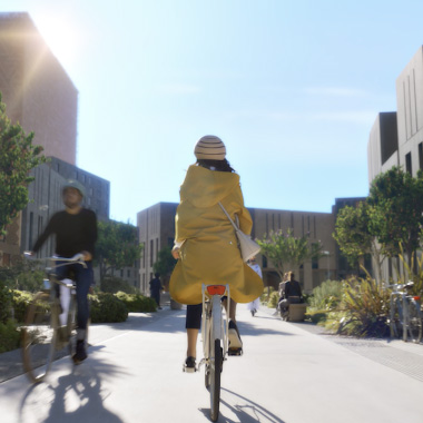 طفل يرتدي معطفًا أصفر يركب دراجة في وسط المدينة الحديث.