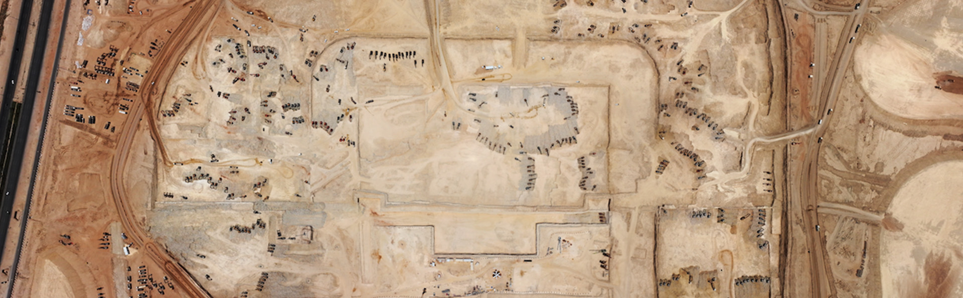 An aerial view of a large construction site in a desert landscape, showing early stages of development with roads and vehicle activity.