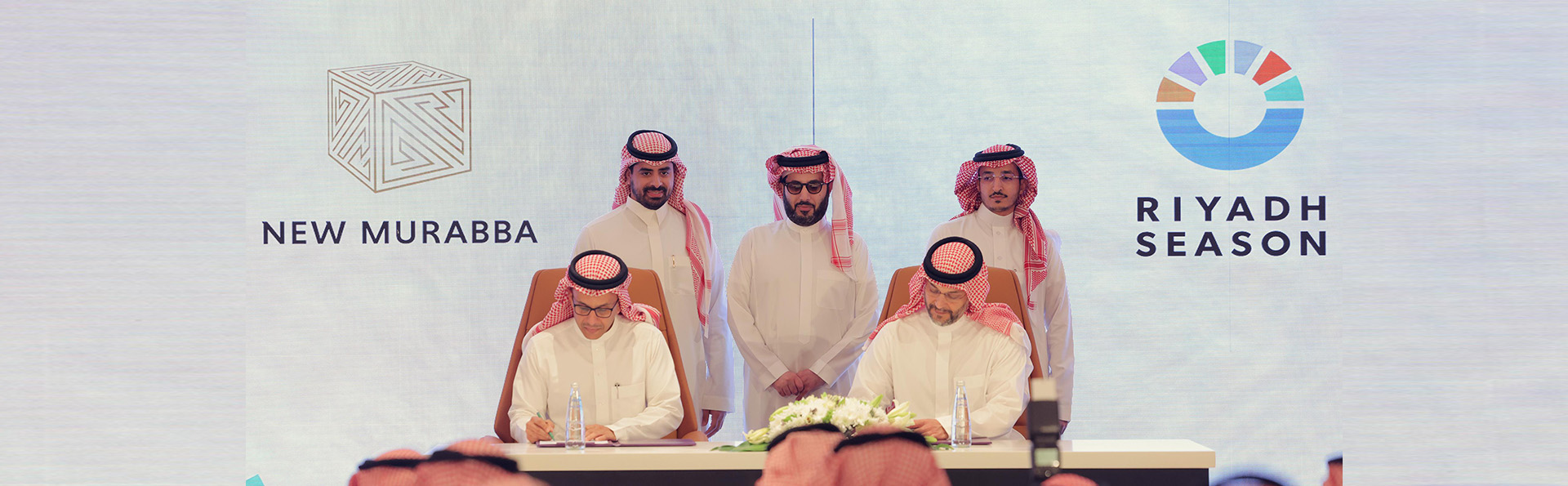 حفل توقيع مع مسؤولين من مشروع المربع الجديد وموسم الرياض كشركاء مميزين رسميين، ويظهر في الصورة رجال سعوديون يرتدون الزي التقليدي.