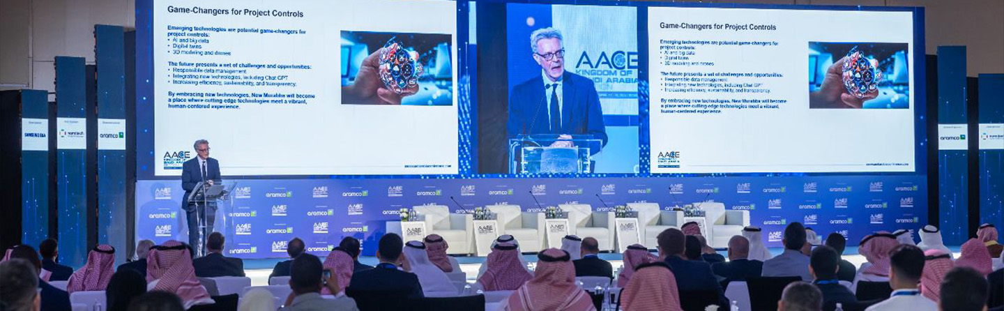 A conference and audience looking on big screen showing a presentation slide about improving project controls